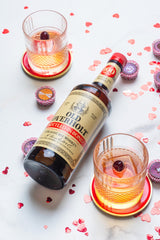 Bottle of Old Overholt Bonded Straight Rye Whiskey on a table next to two cocktails and scattered Valentine's Day decorations.