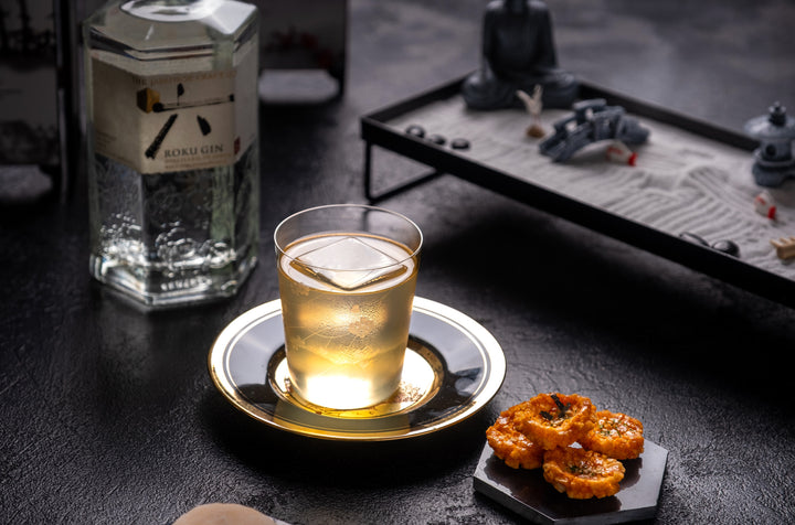 Cocktail in small glass on gold plate sitting on stone countertop.