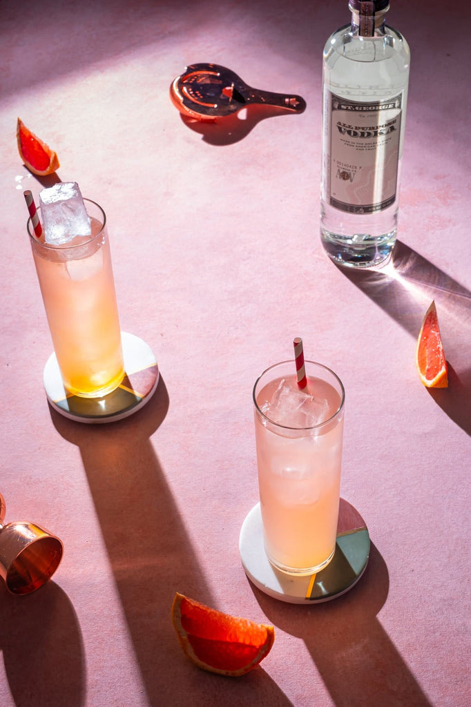 Bottle of St. George All Purpose Vodka on a table next to two cocktails.