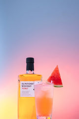 Bottle of Suntory Toki Japanese Whisky next to a cocktail with a watermelon wedge in it.