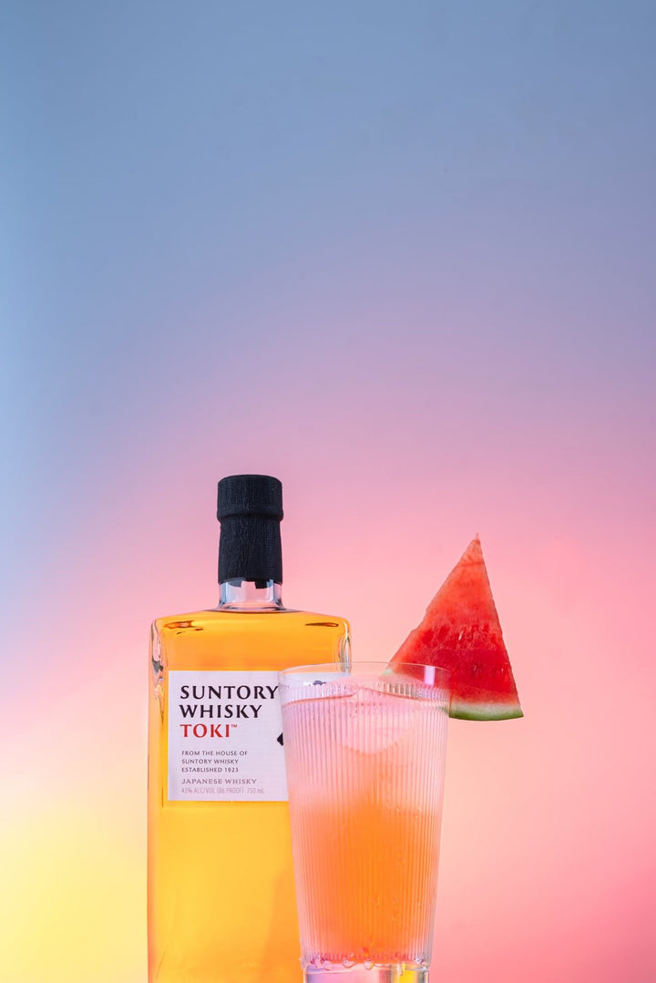 Bottle of Suntory Toki Japanese Whisky next to a cocktail with a watermelon wedge in it.
