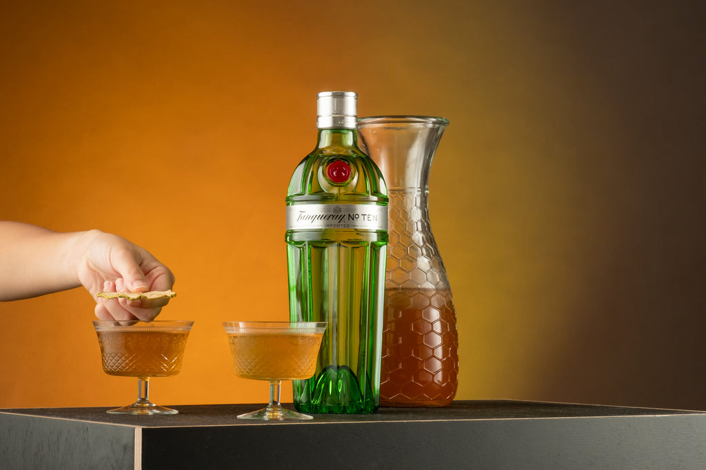 Bottle of Tanqueray No. Ten Gin, sitting on table alongside two poured cocktails.