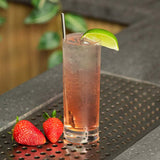 Gin & Tonic Cocktail in a glass with a lime wedge garnish on a bar with Strawberry's next to it.