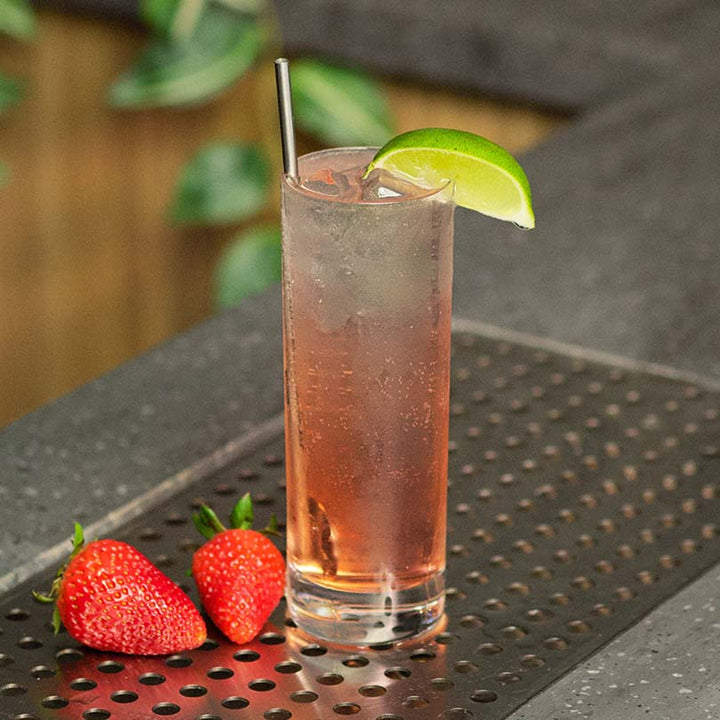 Gin & Tonic Cocktail in a glass with a lime wedge garnish on a bar with Strawberry's next to it.
