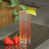 Gin & Tonic Cocktail in a glass with a lime wedge garnish on a bar with Strawberry's next to it.