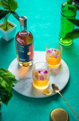 750ml bottle of Ten to One Caribbean Dark Rum on a table next to 2 cocktails.