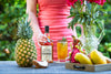 Woman holding a bottle of The Real McCoy 5 Year rum on a picnic table next to cocktail and fruits.