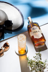 Bottle of Uncle Nearest 1884 Small Batch Whiskey on the ground next to a cocktail, summer hat and sunglasses.
